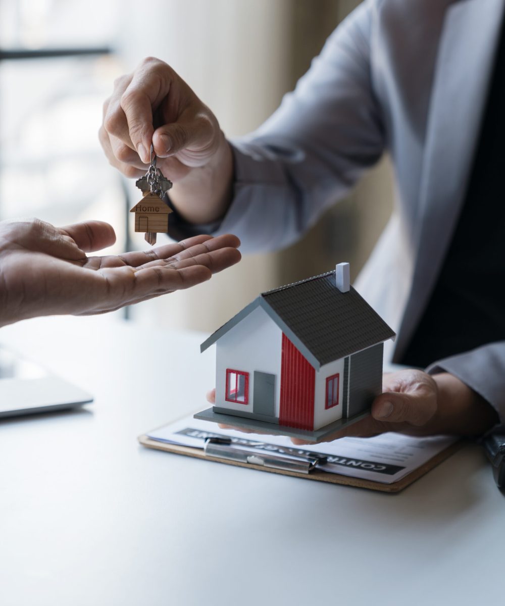 Asian young businessman, architect, engineer handing over house keys on desk in office after agreeing on purchase contract. Or rent to sign a business agreement.