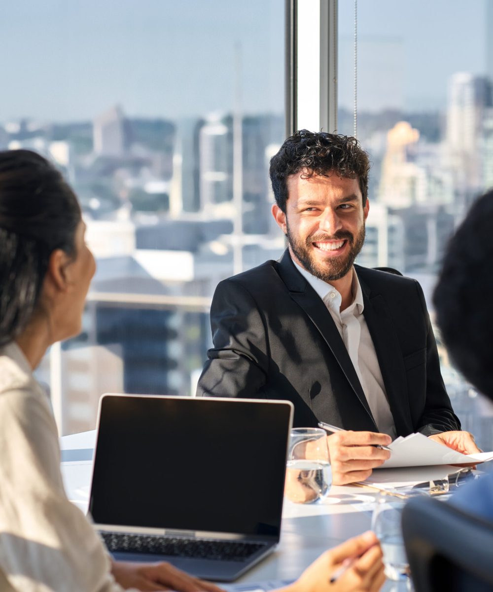 Happy busy professional young latin business man company executive working with team colleagues people discussing project in office at group meeting table in corporate boardroom. Vertical